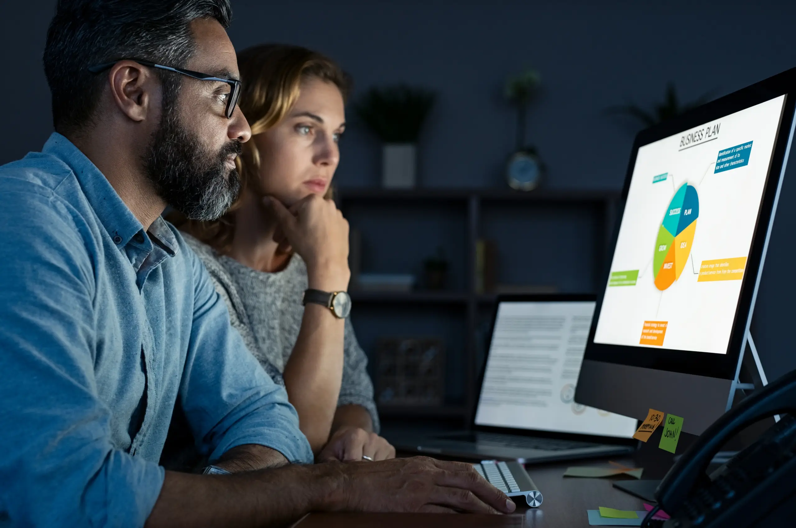 2 people sitting looking at a computer screen with charts on it.