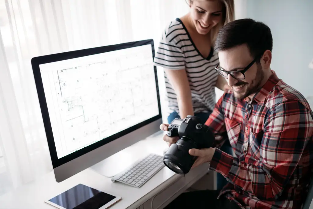 2 people working on a web design in lübeck. sitting in front of computer and looking at the camera for the design