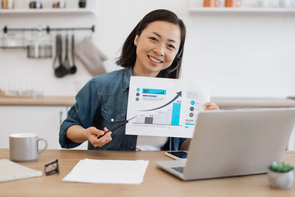 Consultant on a video call holding a growth chart, pointing to a rising conversion graph beside a laptop: CRO results.