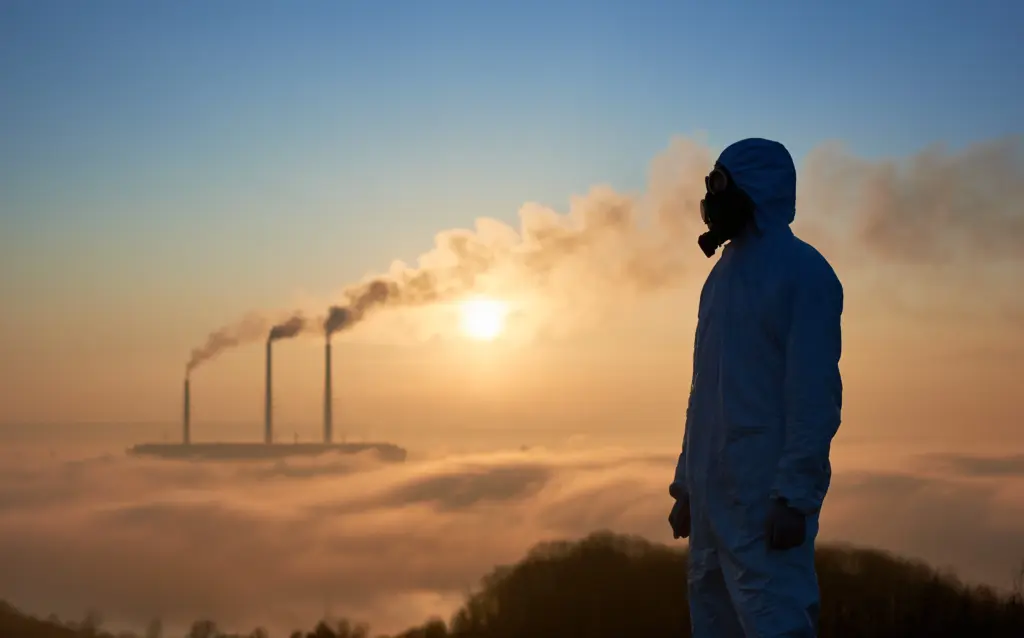 Silhouette of a person in protective gear looking at smokestacks at sunrise, representing our commitment to permanent carbon removal.