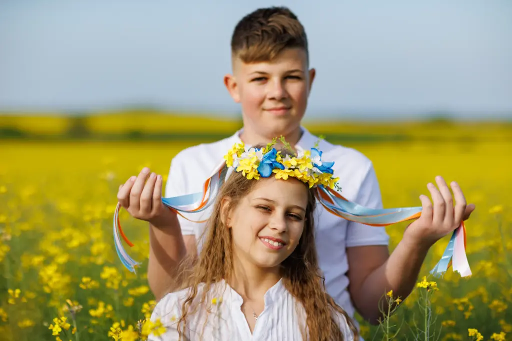 Girl wearing a blue and yellow floral wreath with ribbons in a yellow field, with an older boy behind her, for The WebDev article on the We Are All Ukrainians USA website redesign.