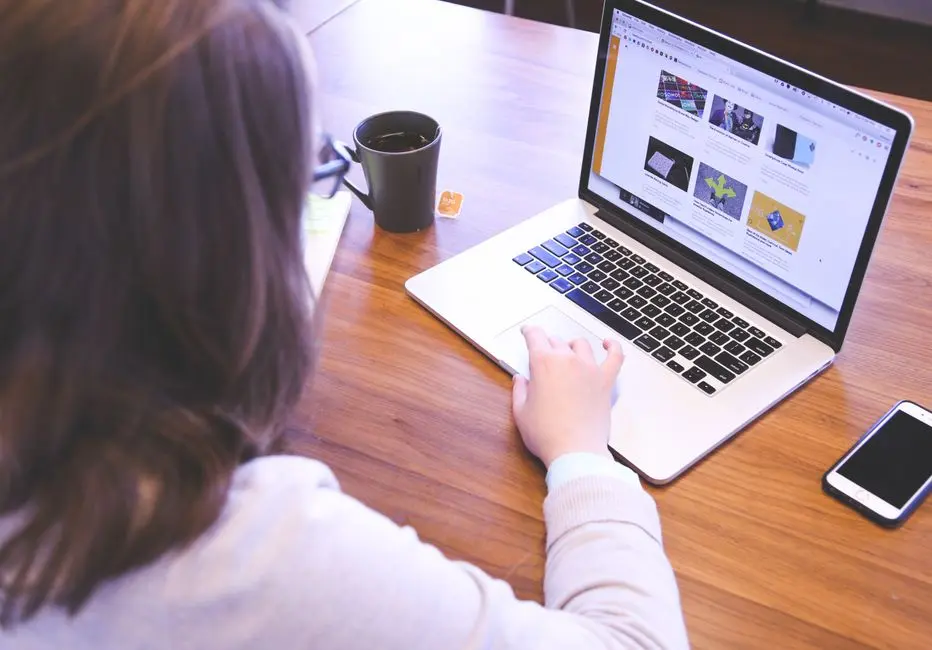 Frau von hinten betrachtet eine Website auf ihrem Laptop am Schreibtisch, genau das entscheidet was deine Website in 5 Sekunden kommuniziert.